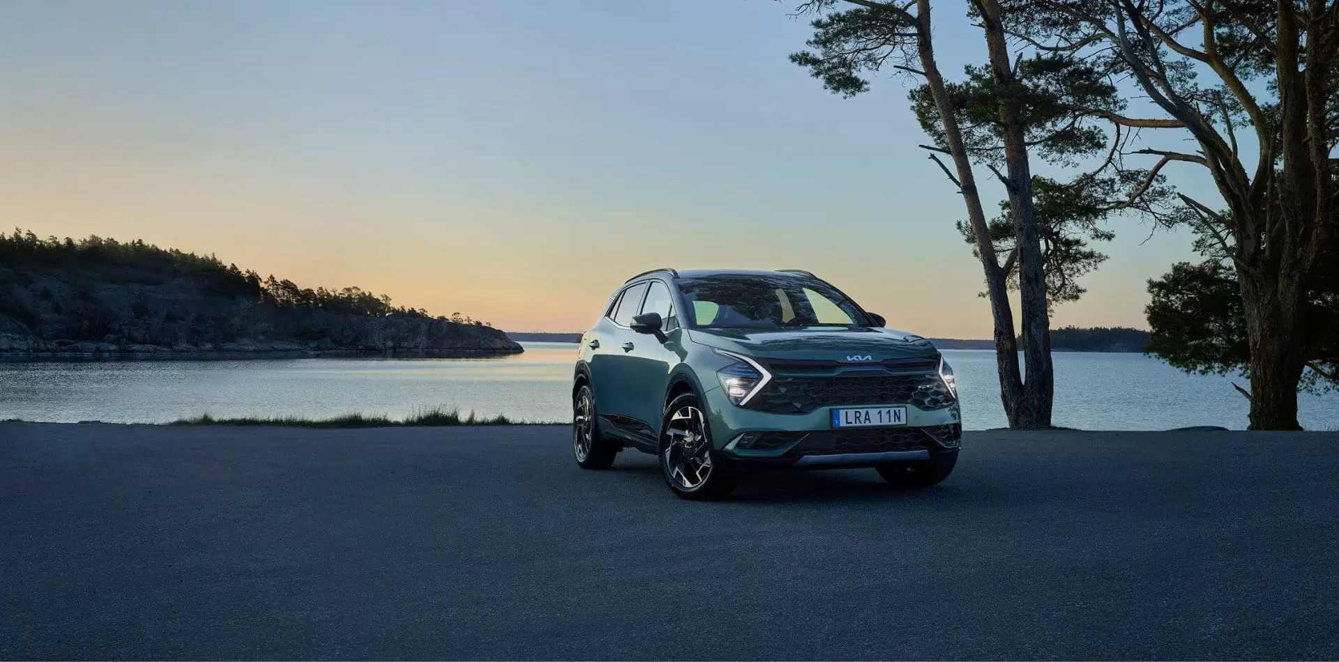 Kia Sportage Plugin-hybrid parkerad på grusplan i solnedgång framför en sjö